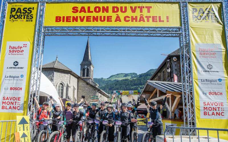 Pass’Portes du Soleil MTB event in Châtel, France – Mountain bikers posing at the VTT expo entrance with alpine views and event banners. A top festival for MTB enthusiasts in the French Alps.